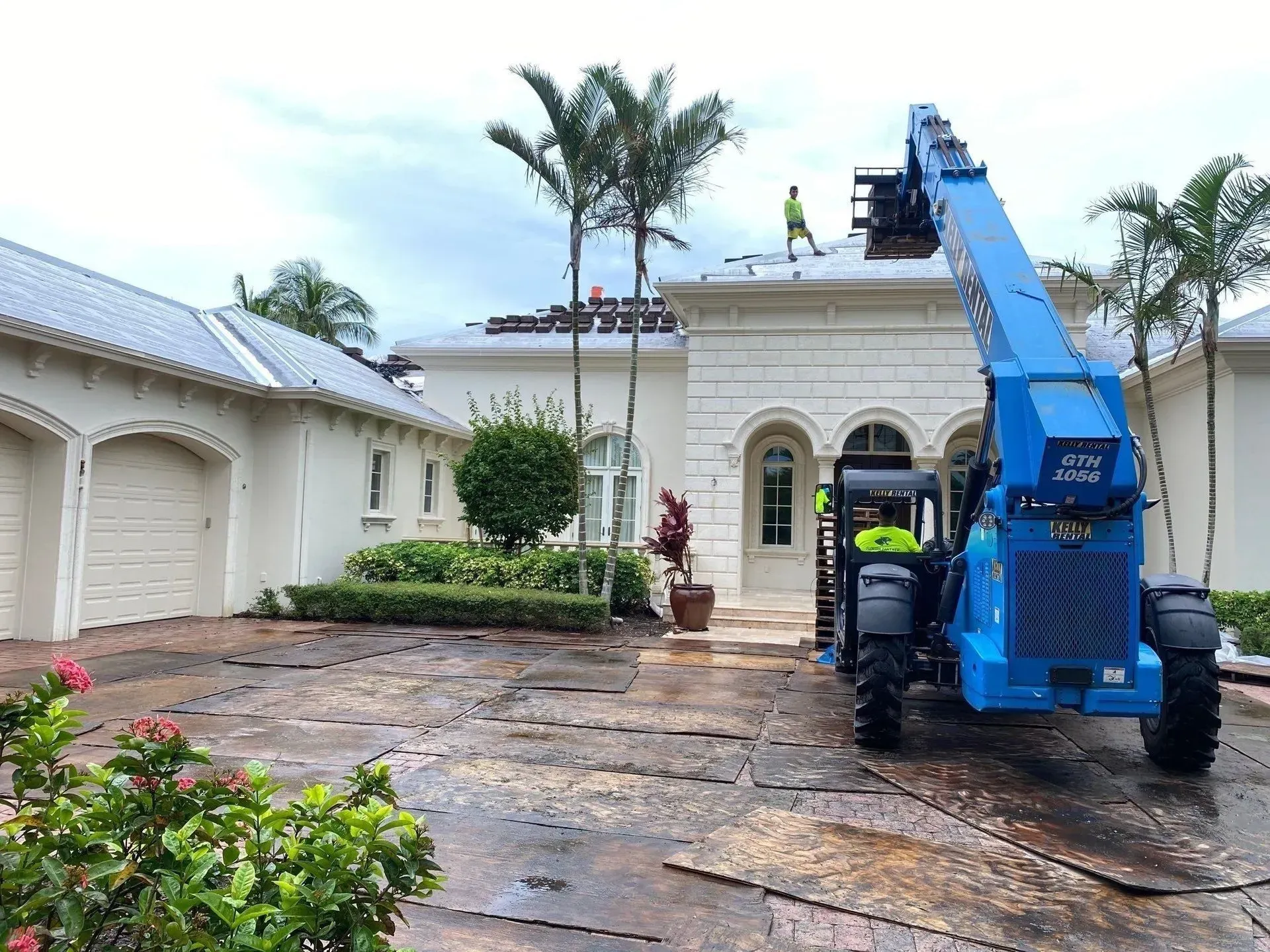 Blue cherry picker lifting workers on a driveway outside a large white house