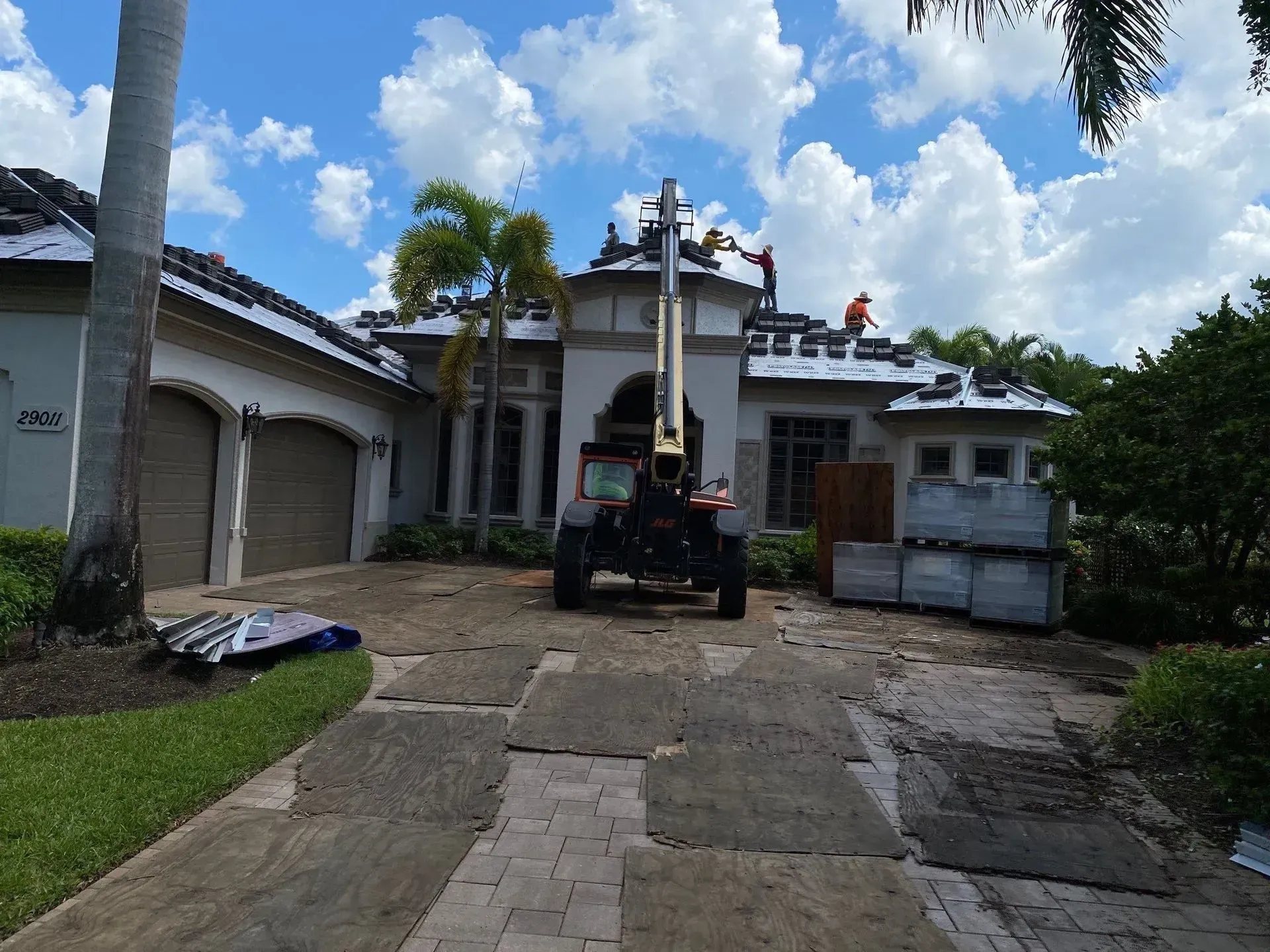 Rough concrete driveway leading to a white house with a large roof repair lift under a blue sky.