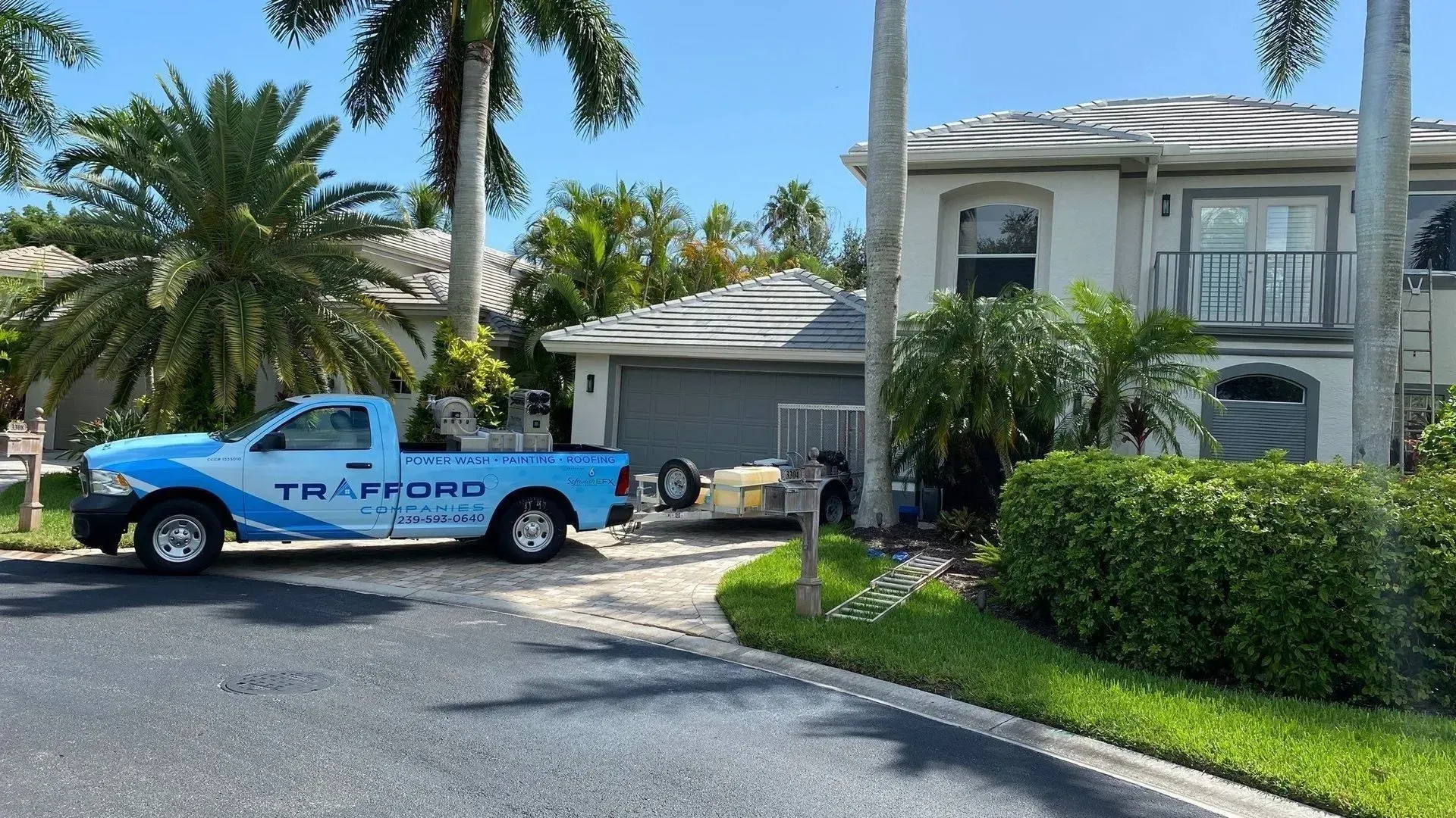 Blue landscaping truck parked by a palm-lined house driveway on a sunny day