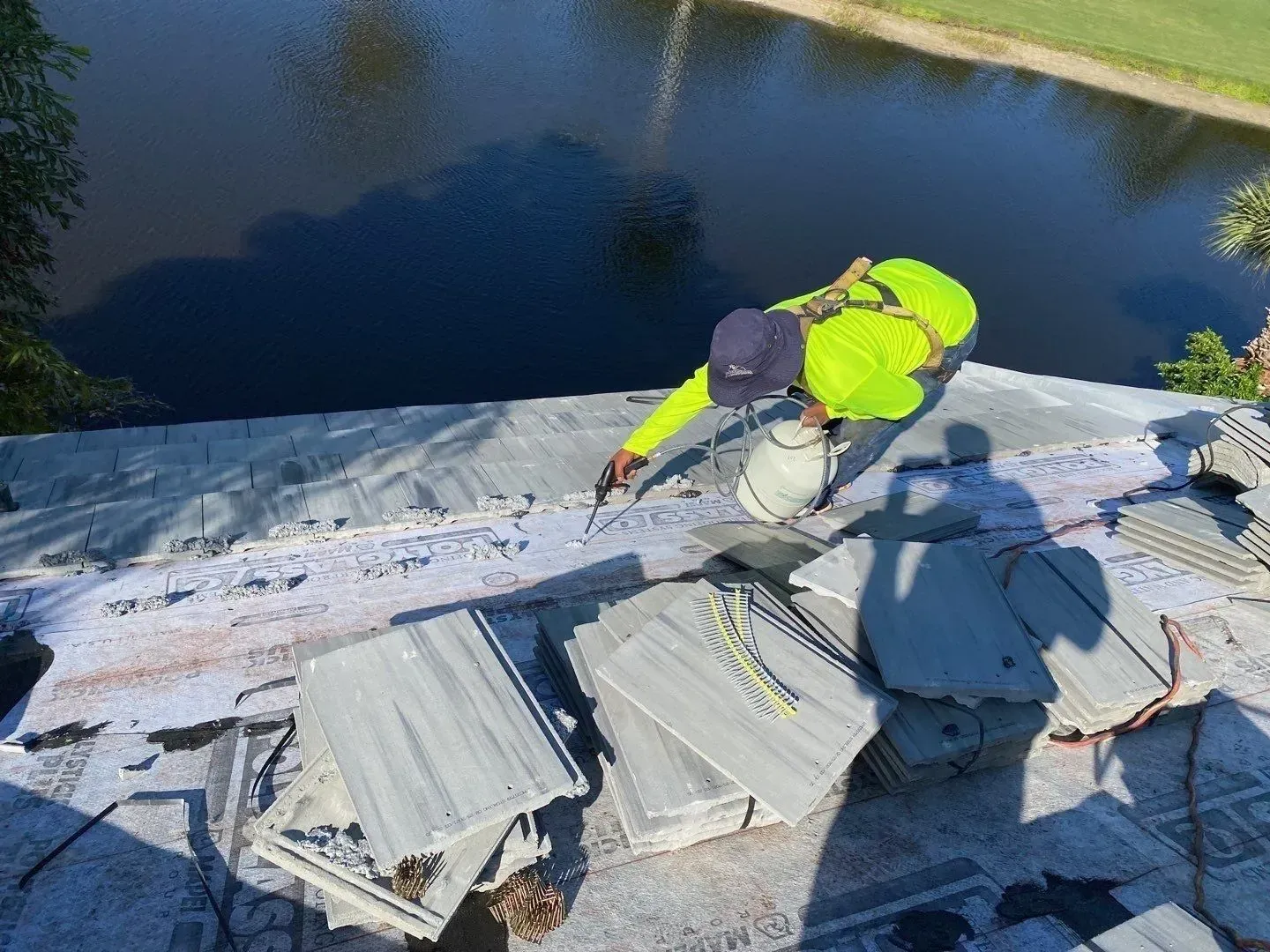Worker in neon jacket on a roof repairing shingles beside a pond