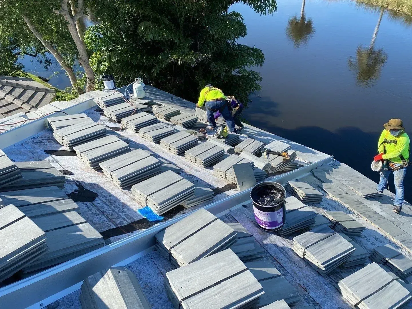 Workers loading white rectangular blocks on a flatboat beside calm water and trees