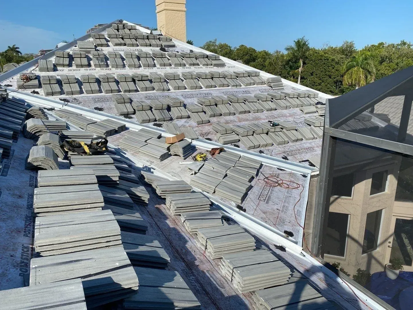 Partially damaged roof with stacked shingles and debris under a clear blue sky