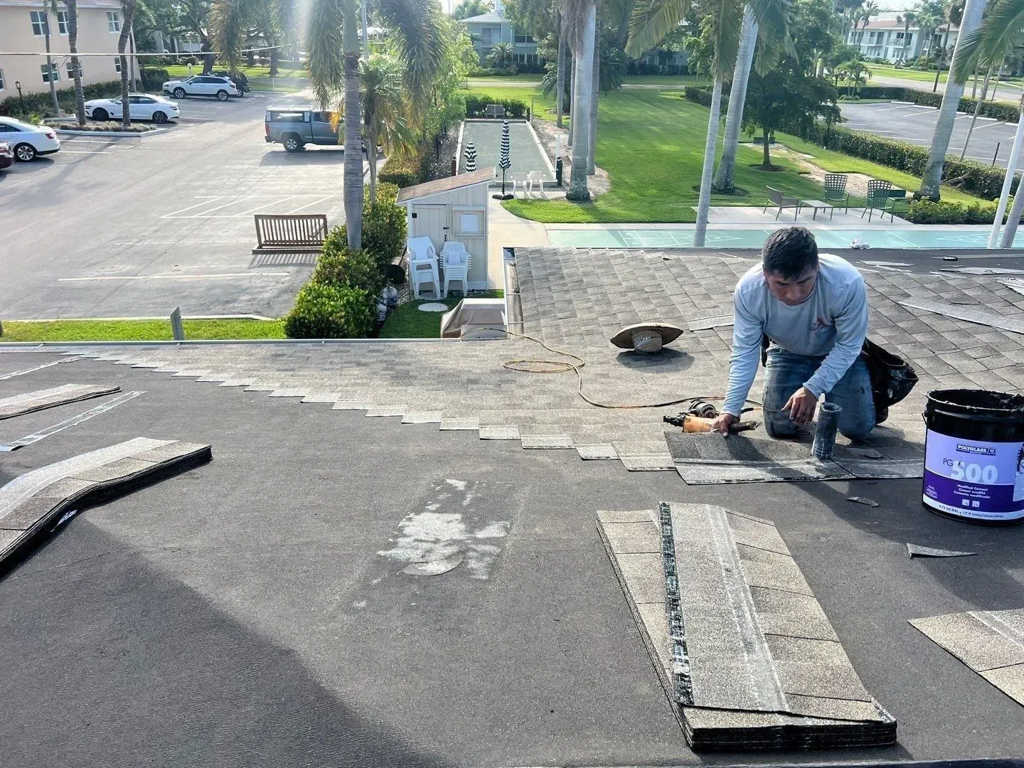 Worker kneeling on a rooftop, applying sealant near a vent with tools and a bucket nearby.