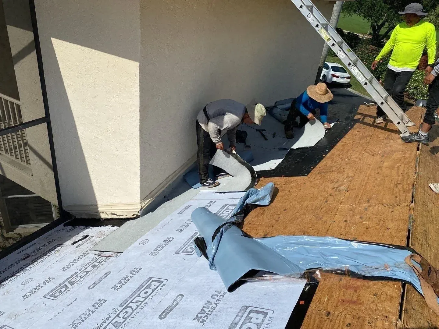 Workers installing roofing underlayment on a sloped roof beside a building wall