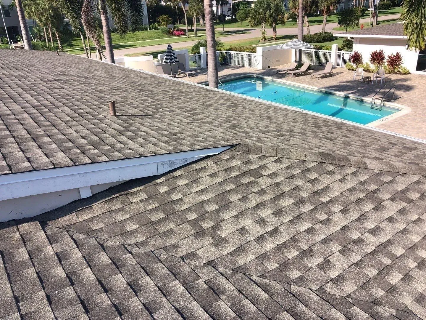Shingled rooftop beside a turquoise swimming pool and patio area.