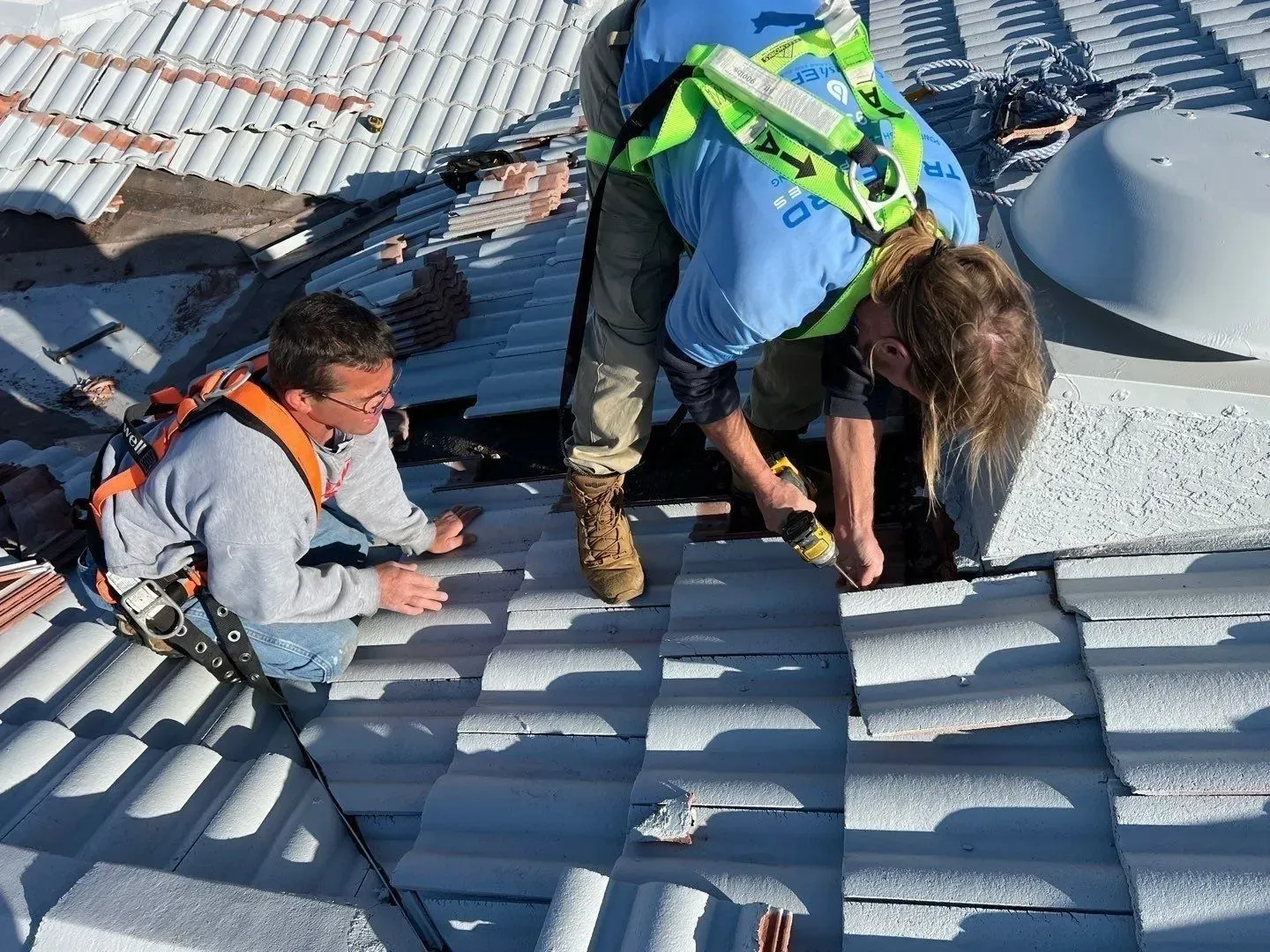 Workers inspecting a gray metal roof, one crouched and two bent over near the ridge line