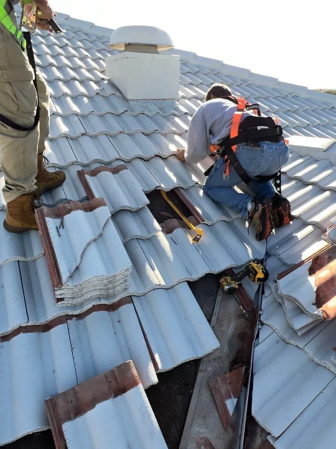 Two workers repairing a tiled roof with safety harnesses on a steep rooftop.