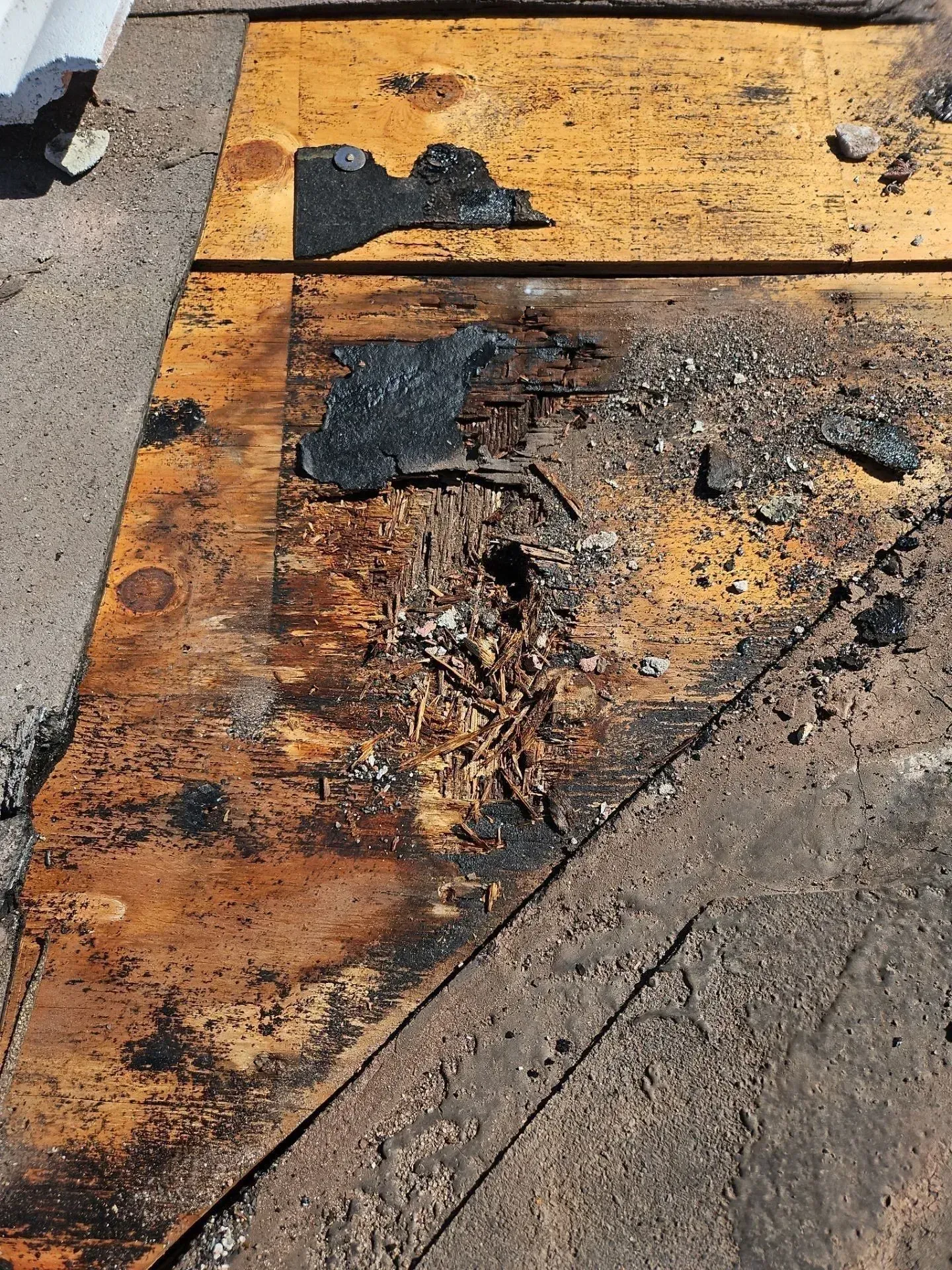 Damaged orange and black painted surface with peeling, rust, and cracks beside a concrete edge
