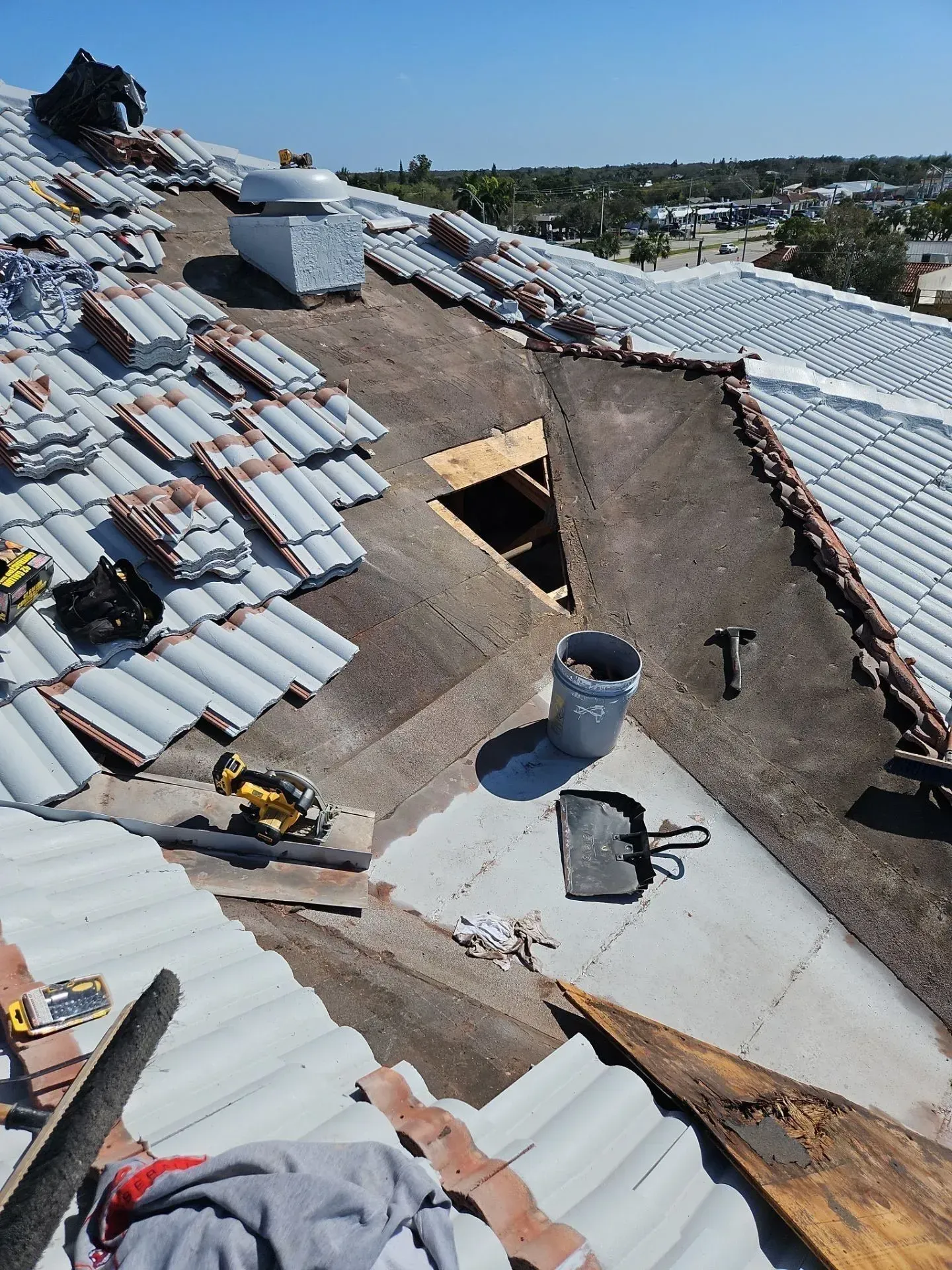 Roof under repair with white tiles, exposed underlayment, and a worker on a sloped rooftop.
