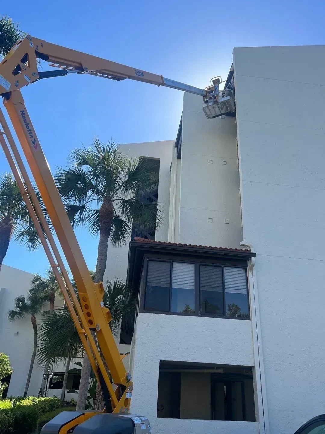 Yellow crane lifting debris beside a white building under a clear blue sky.