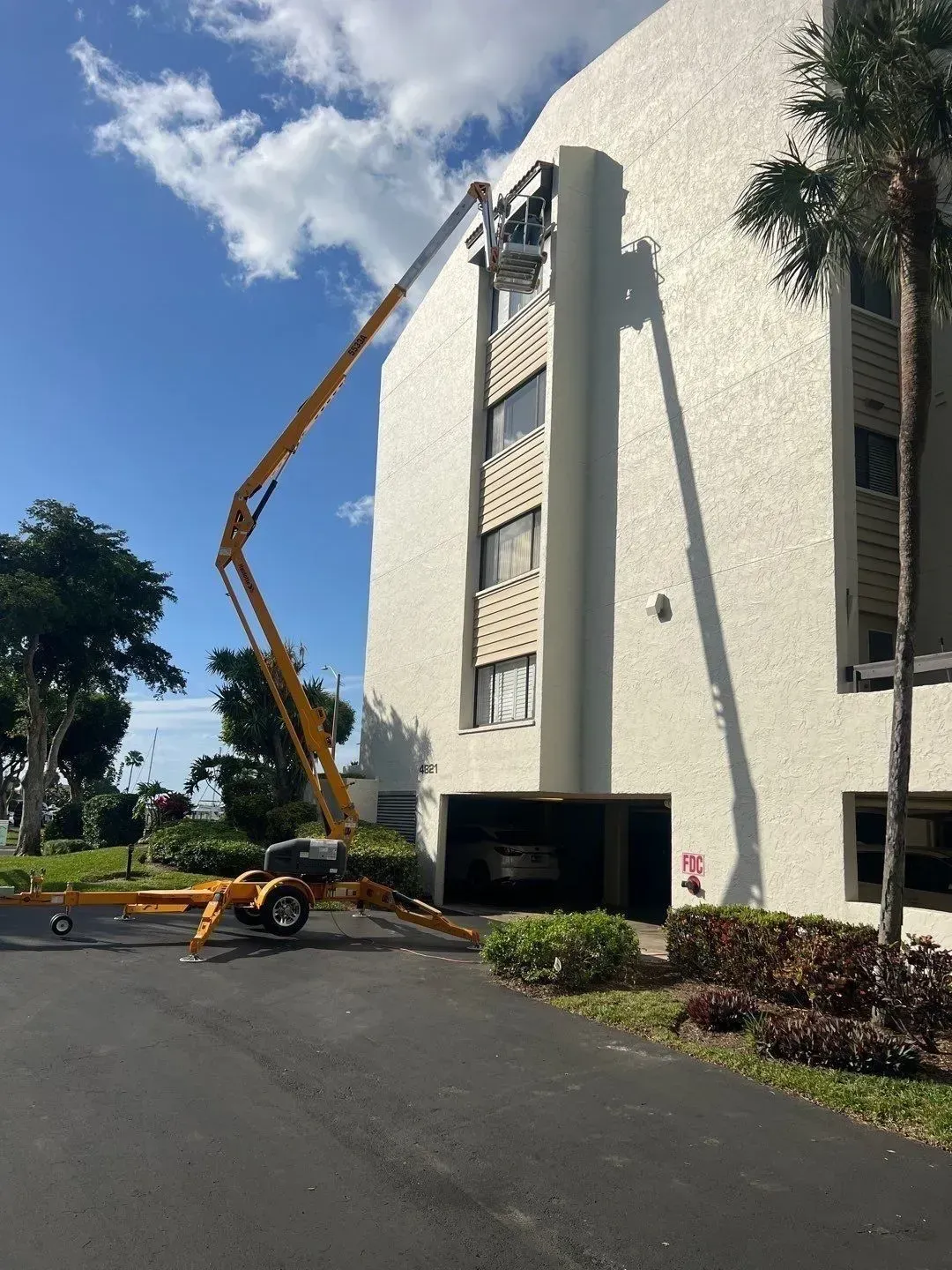 Aerial lift beside a white apartment building, reaching up toward a window under a blue sky.
