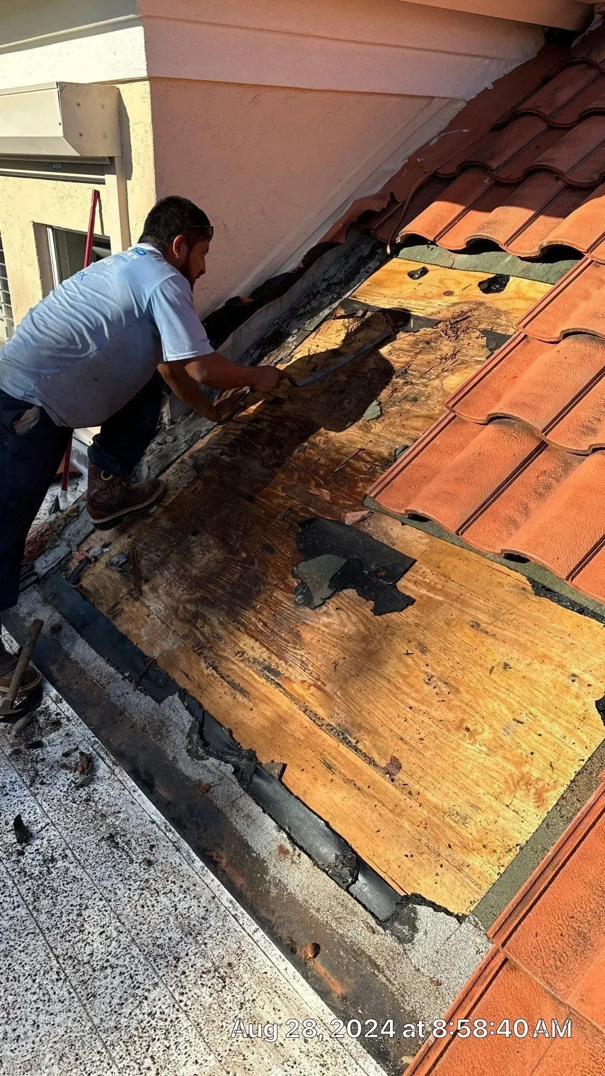 Worker repairing a damaged tile roof with exposed underlayment and dark water stains
