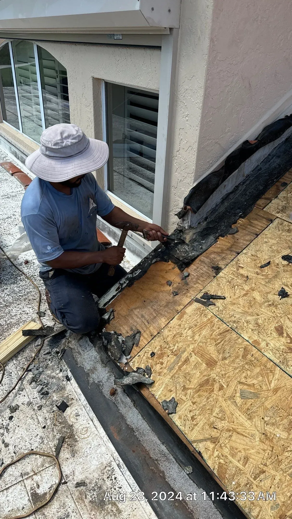 Worker repairing roof flashing along a wall on a sloped rooftop.