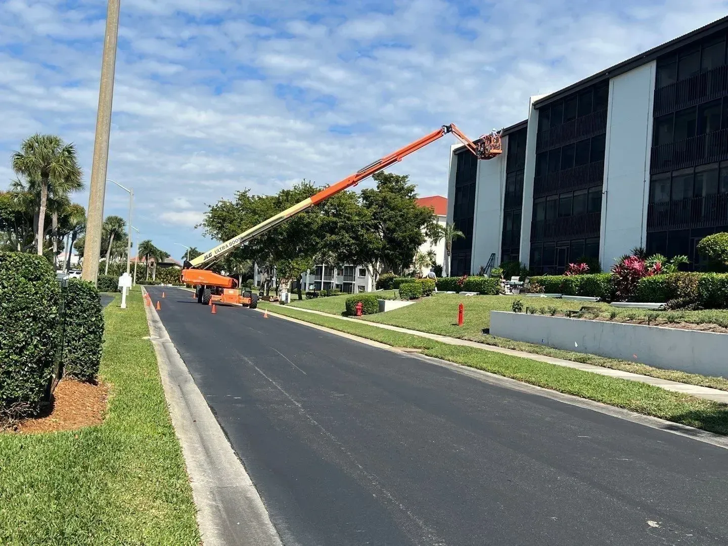 Orange cherry picker beside a modern black building on a landscaped road under a partly cloudy sky