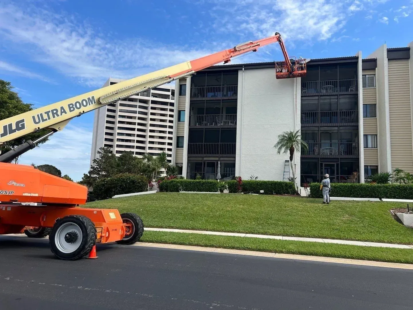Orange boom lift reaching building roof beside a modern office block under a blue sky