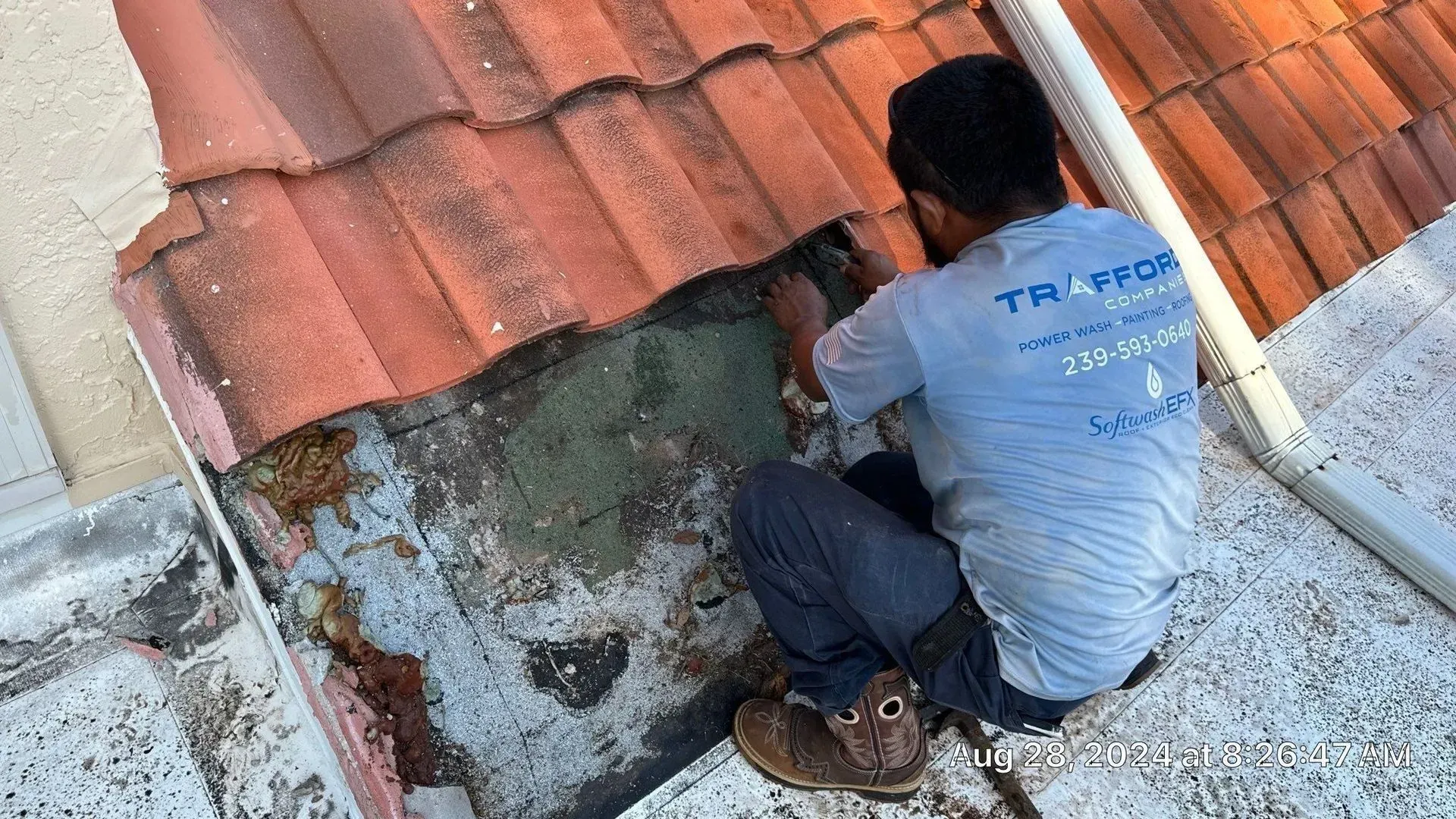 Worker repairing damaged roof tiles on a rooftop, crouched beside a broken patch and gray waterproofing.
