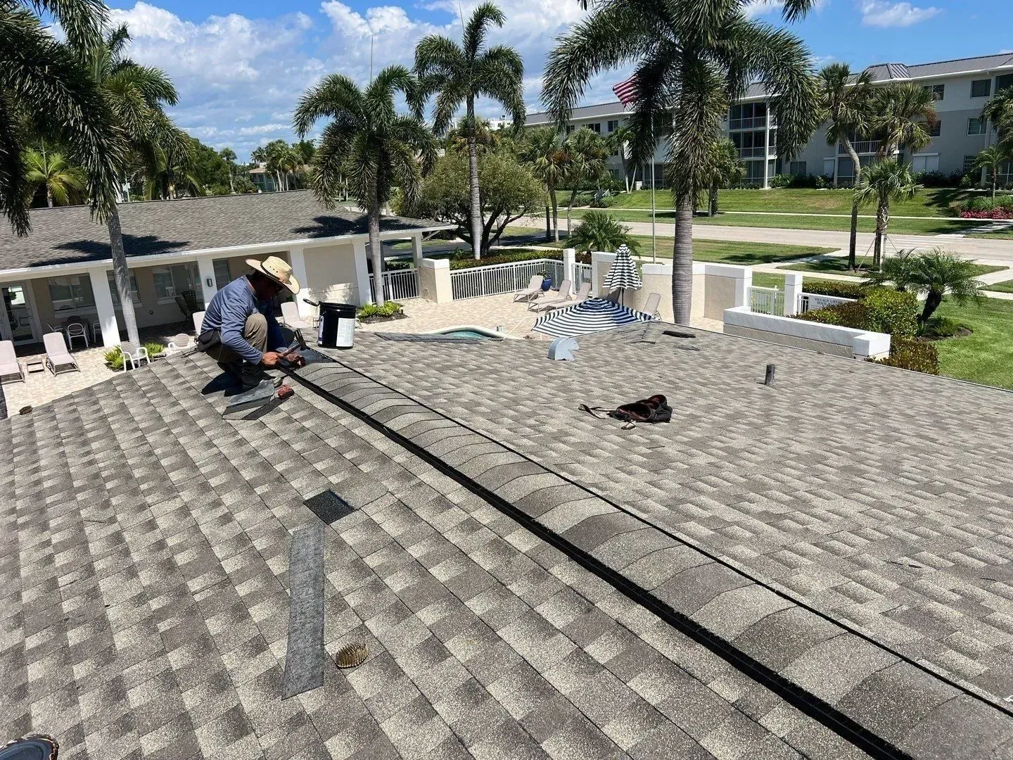 Workers repairing a flat roof on a sunny residential building, with palm trees in the background
