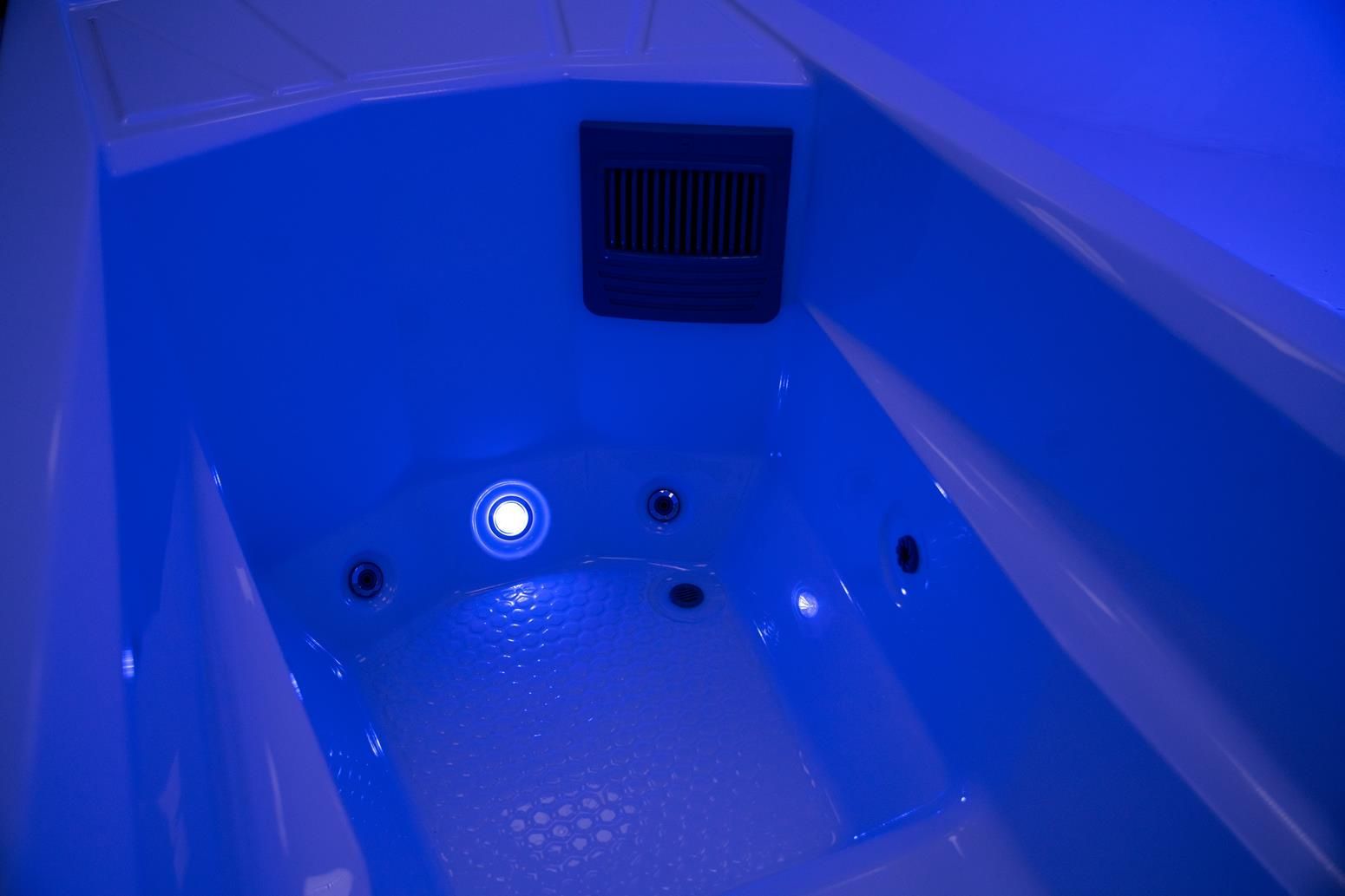 A blue-lit, empty jacuzzi tub with jets and a vent.
