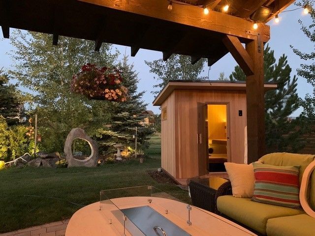 Backyard scene with a sauna, seating area, and a fire pit at dusk.