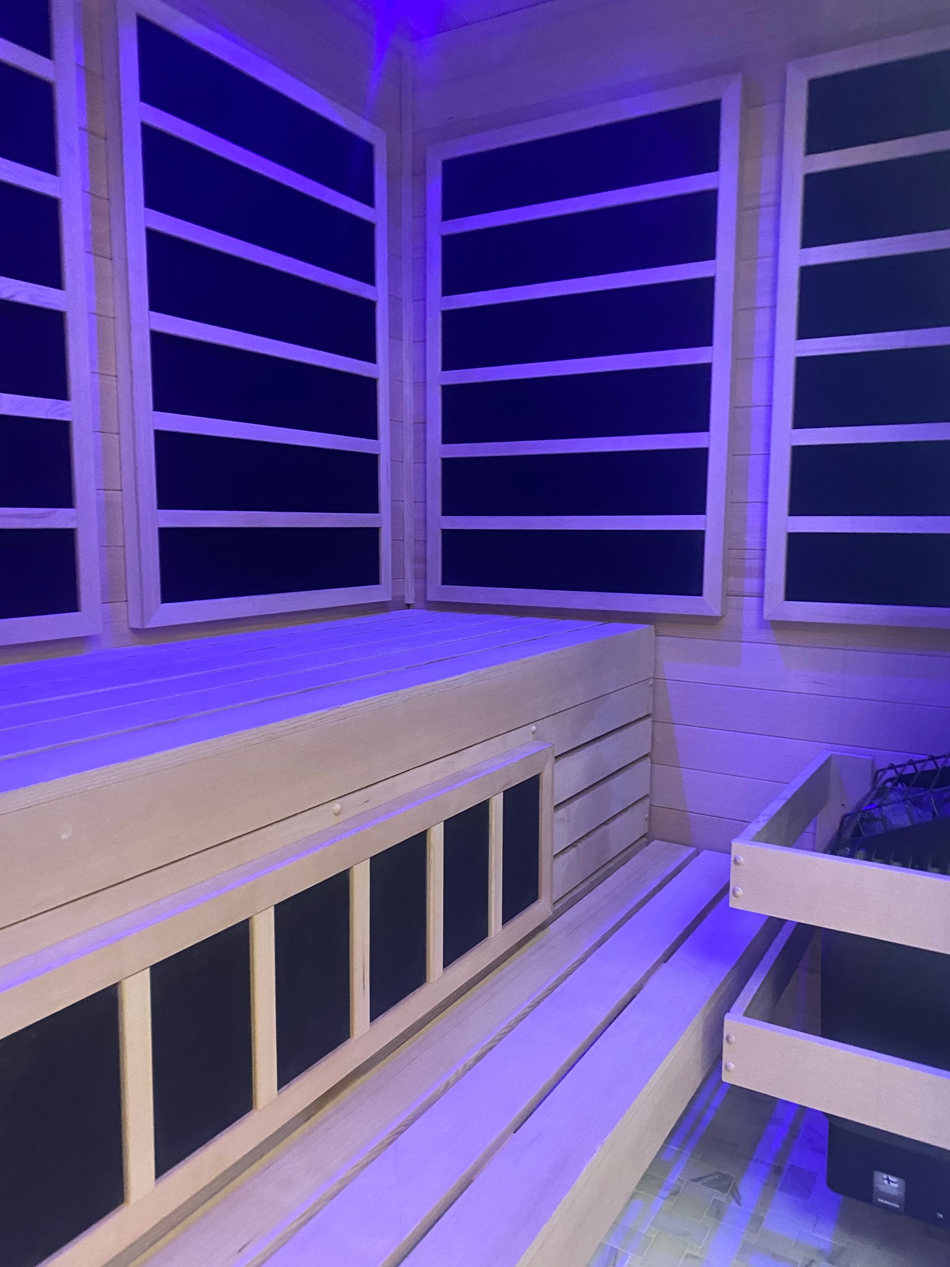 Wooden sauna interior with blue lighting, benches, and black panel heaters.