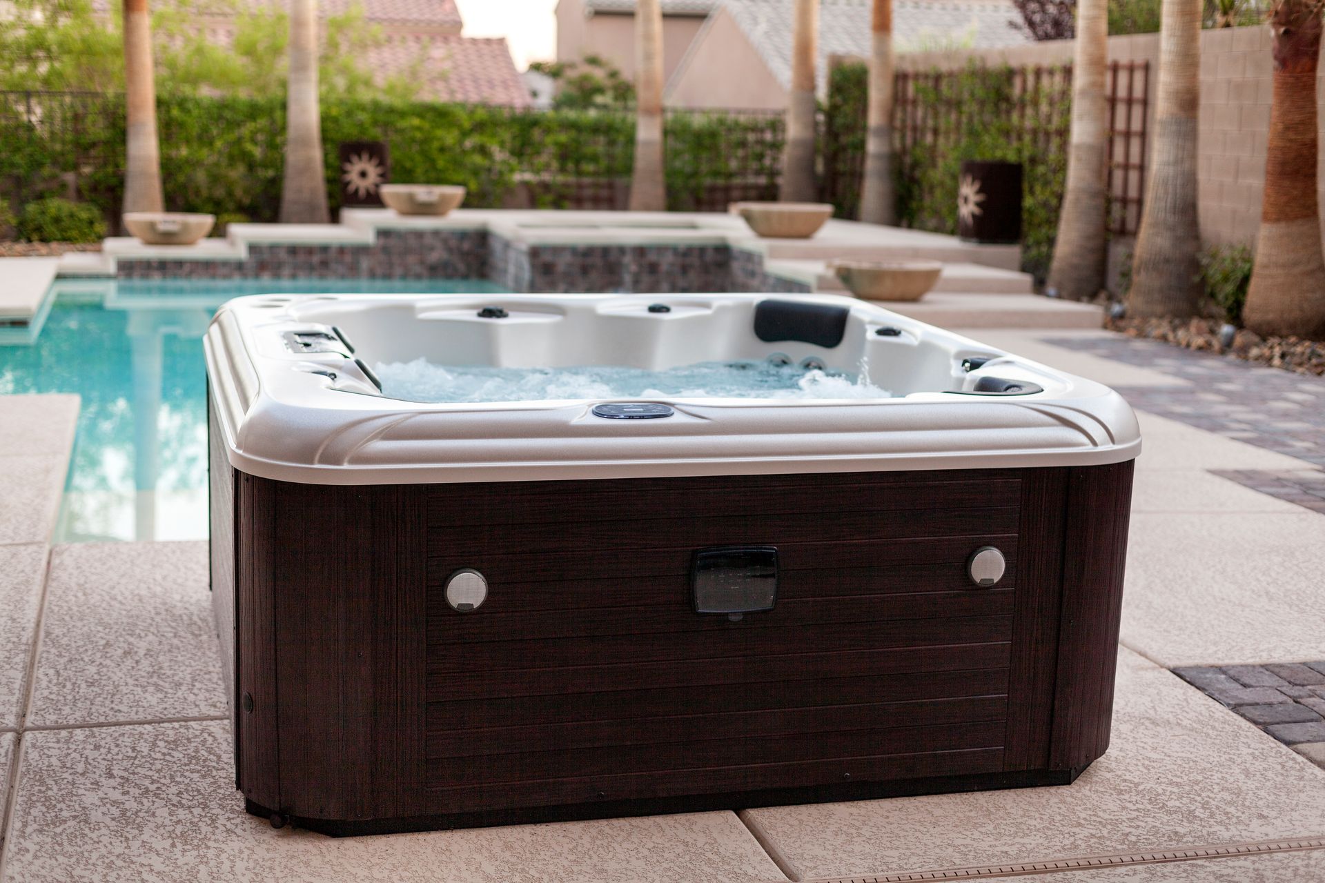 Hot tub, brown siding, next to a pool. Palm trees in the background, sunny day.