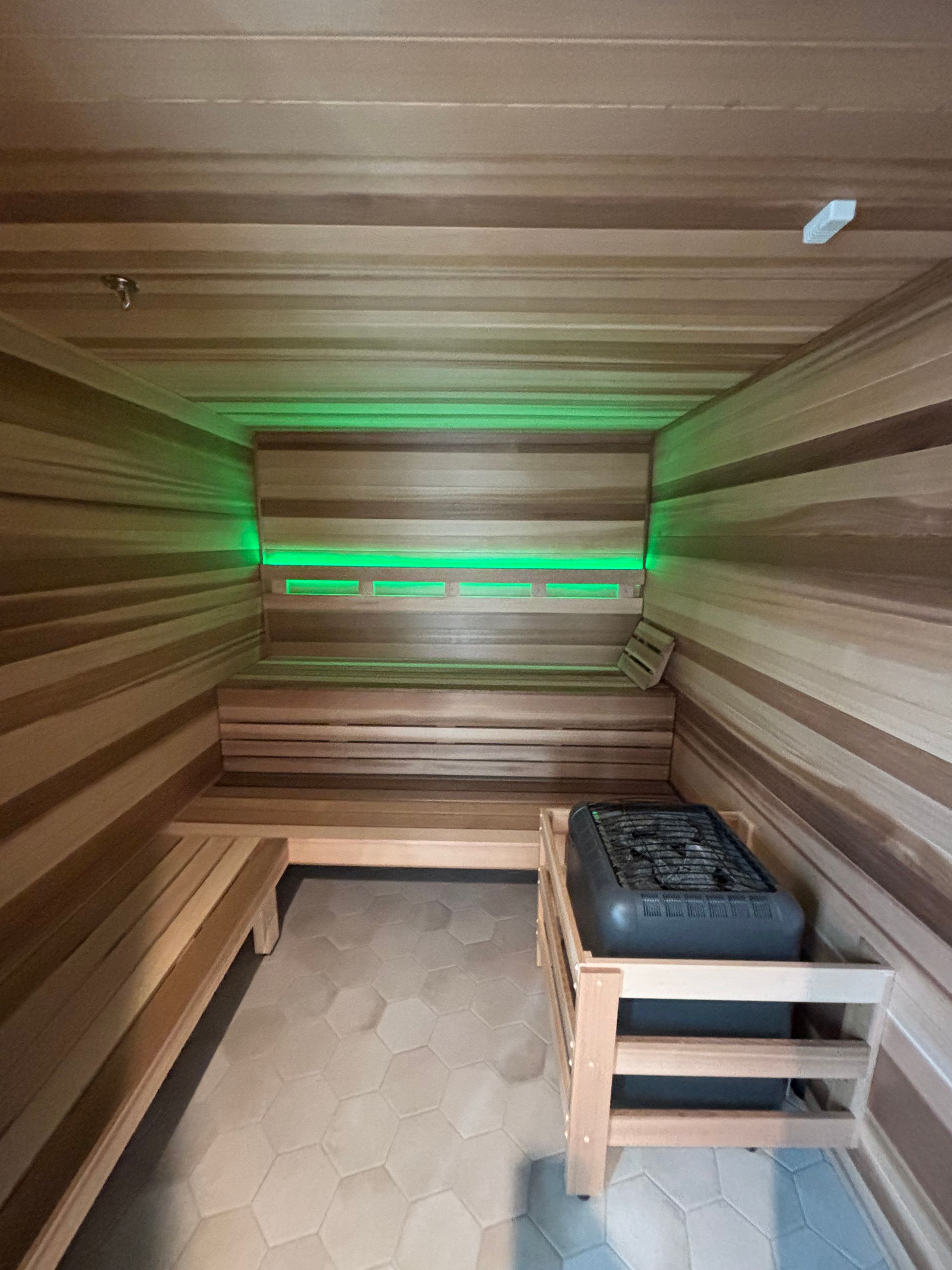 Wood-paneled sauna with bench seating and green backlighting