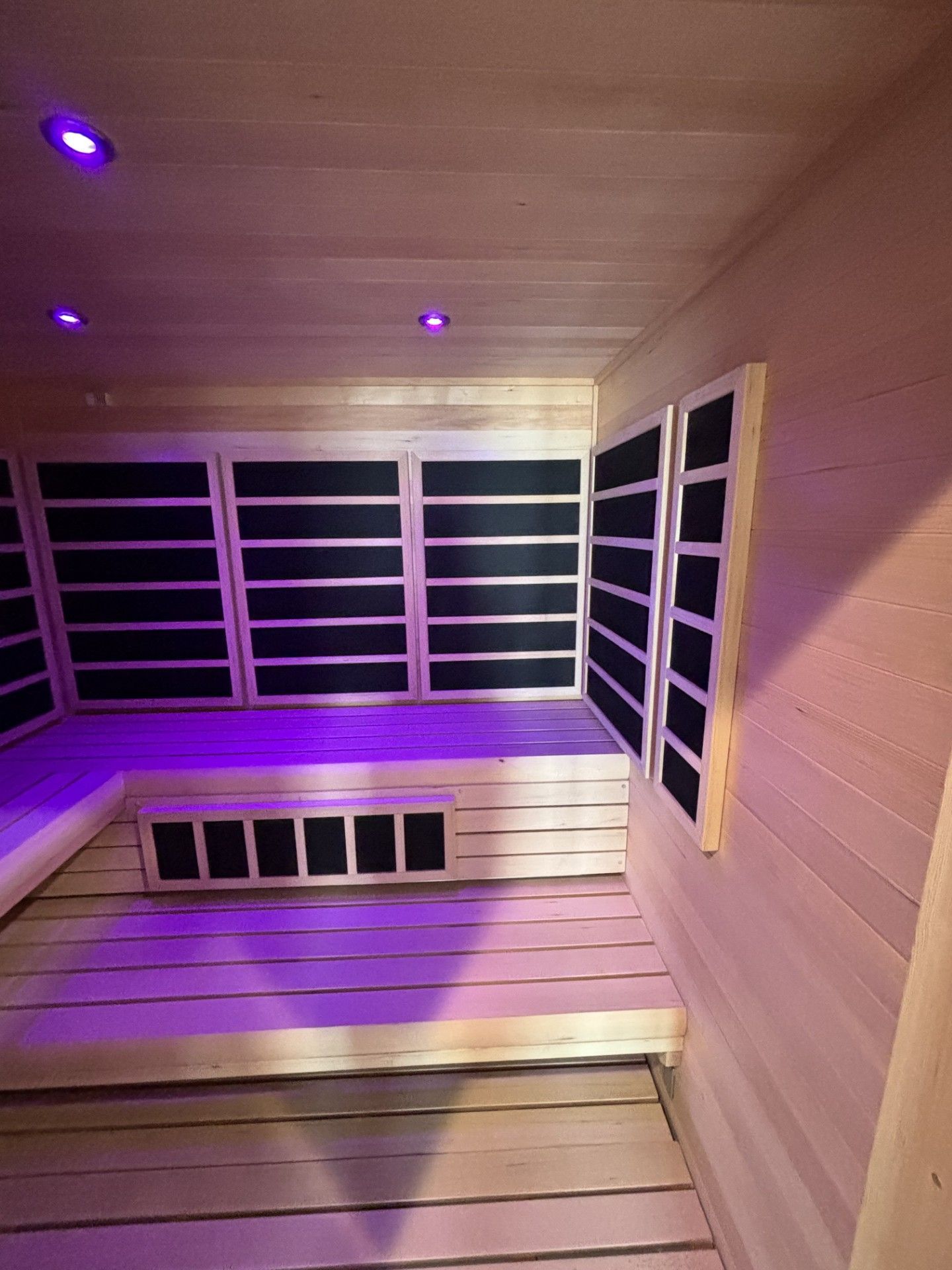 Interior of a sauna with light wood paneling, black heating elements, and purple overhead lighting.