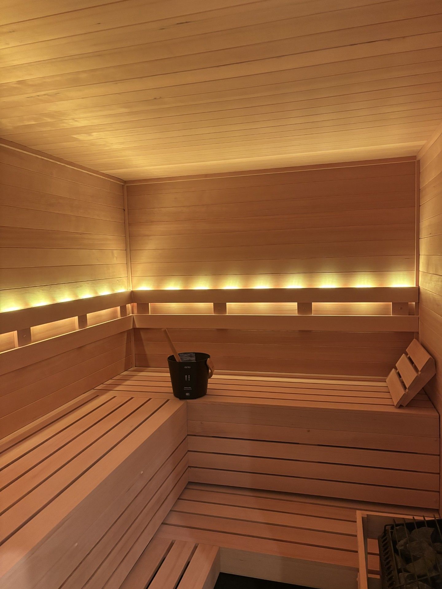 Wooden sauna interior with benches, bucket, and ambient lighting.