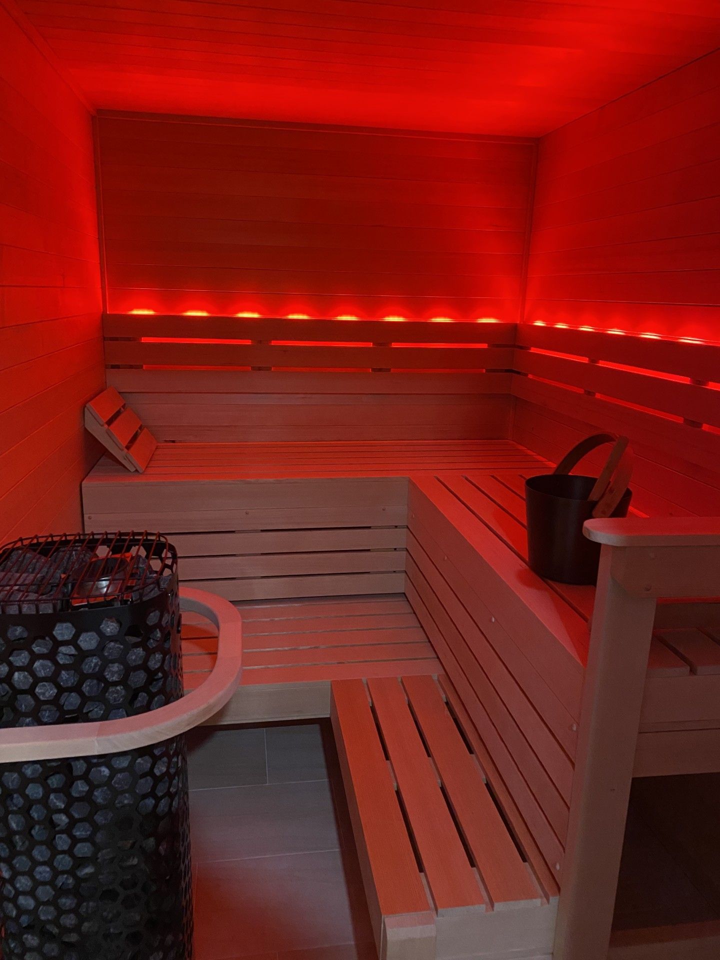 Interior of a sauna with wooden benches, red lighting, and a bucket.