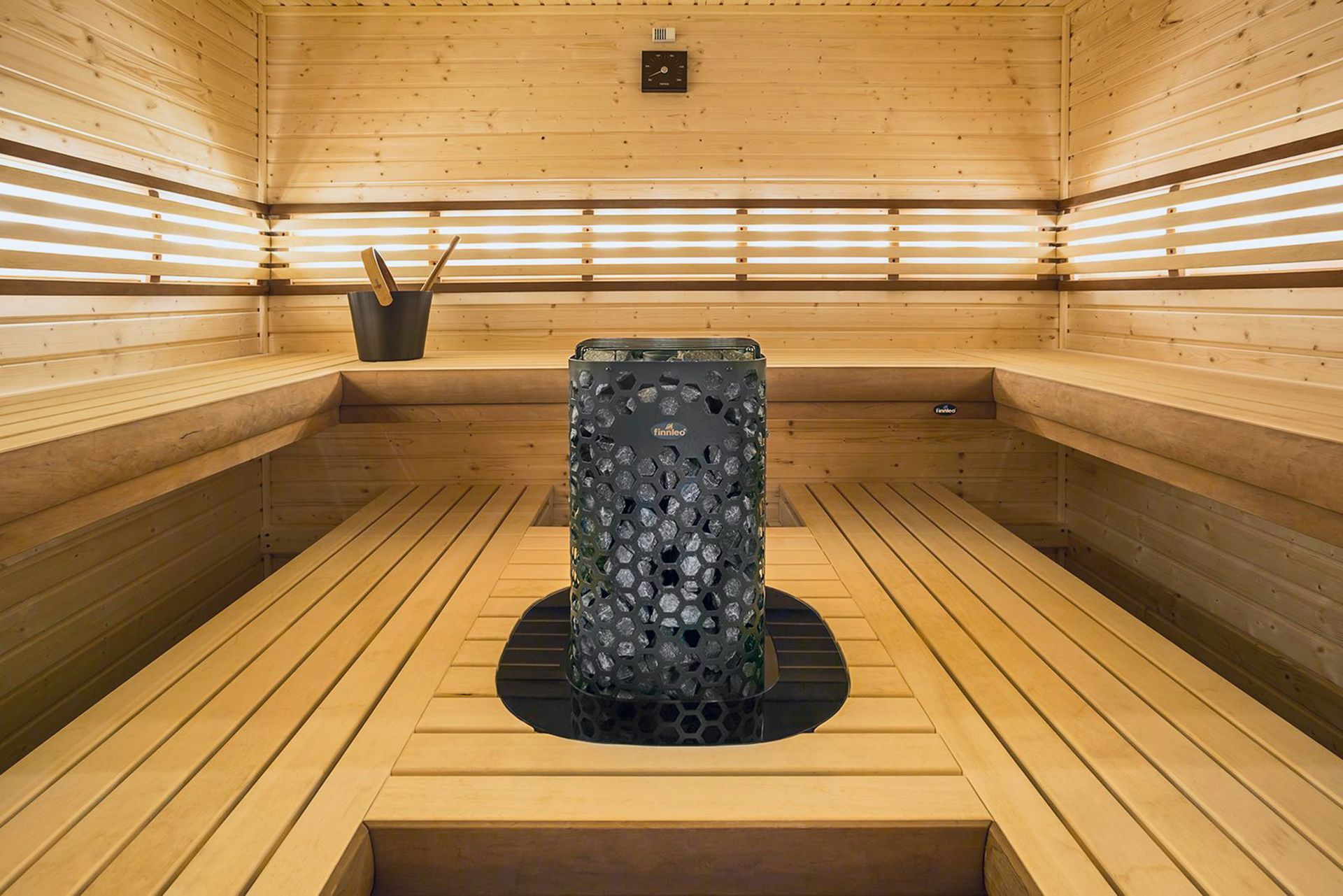 Inside a sauna with wooden benches, a heater, and a bucket.