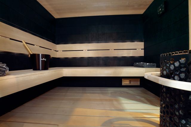 Interior of a sauna with wooden benches and dark walls; a bucket and stones are visible.