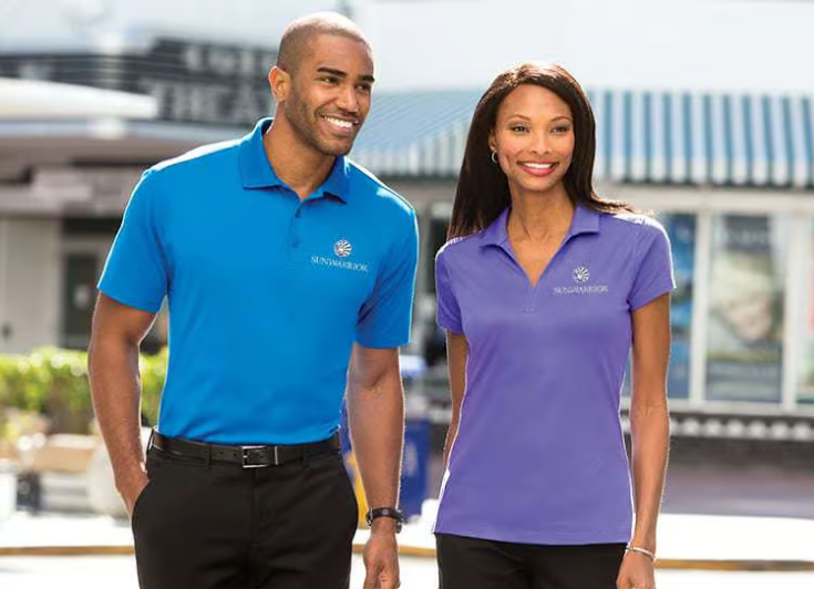 Two smiling employees in blue and purple polos walking outside a building.