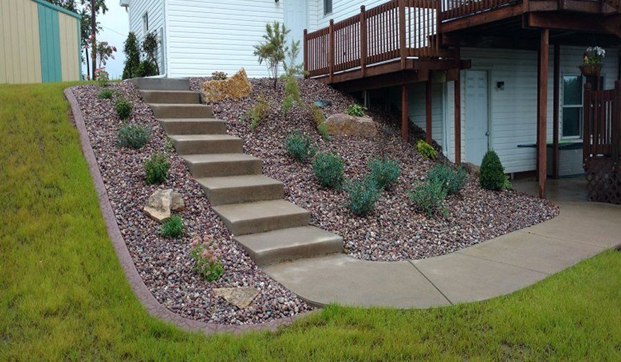 Concrete steps and rock garden lead up a hill to a house's upper level and deck.