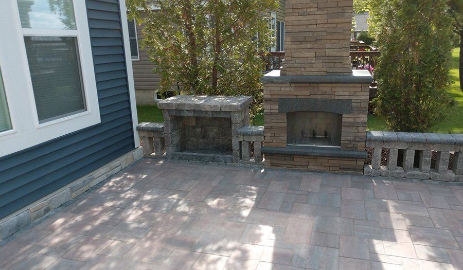 Brick patio with outdoor fireplace and wall adjacent to a house with blue siding.