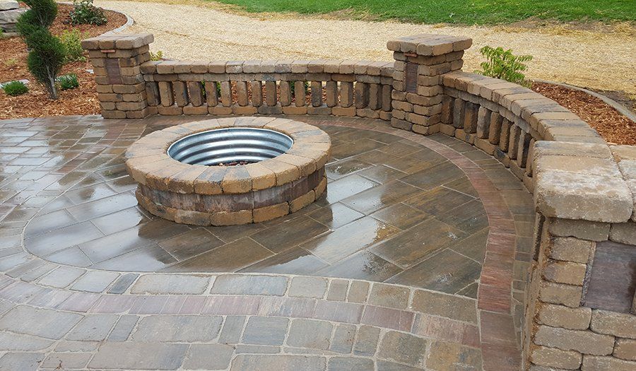 Stone patio with fire pit, curved wall, and decorative pillars. Wet bricks reflect the sky.