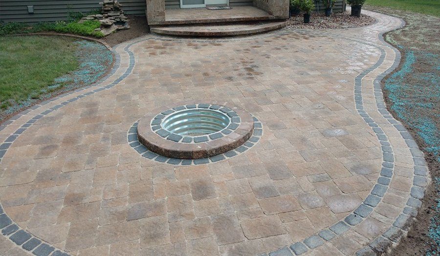 Brick patio with a built-in fire pit. A wavy, dark border surrounds the light-colored bricks.