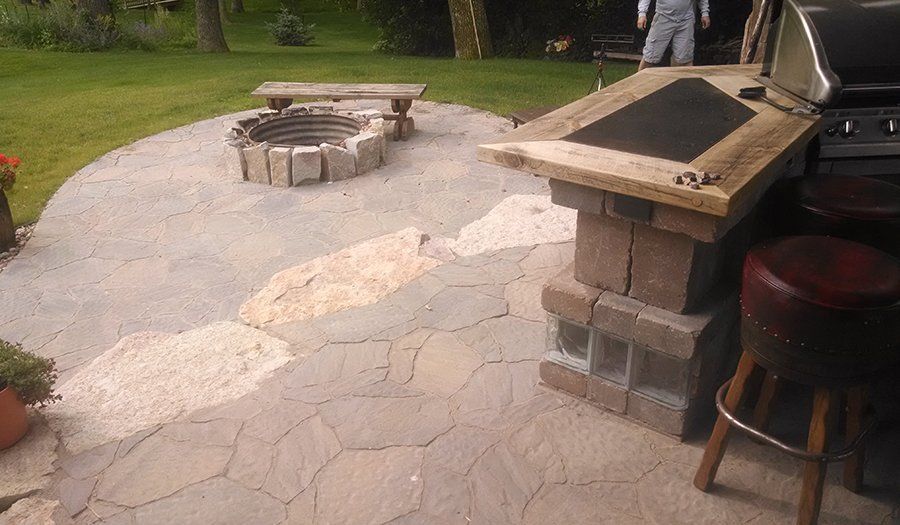 Stone patio with fire pit and outdoor kitchen, featuring a grill and bar seating.