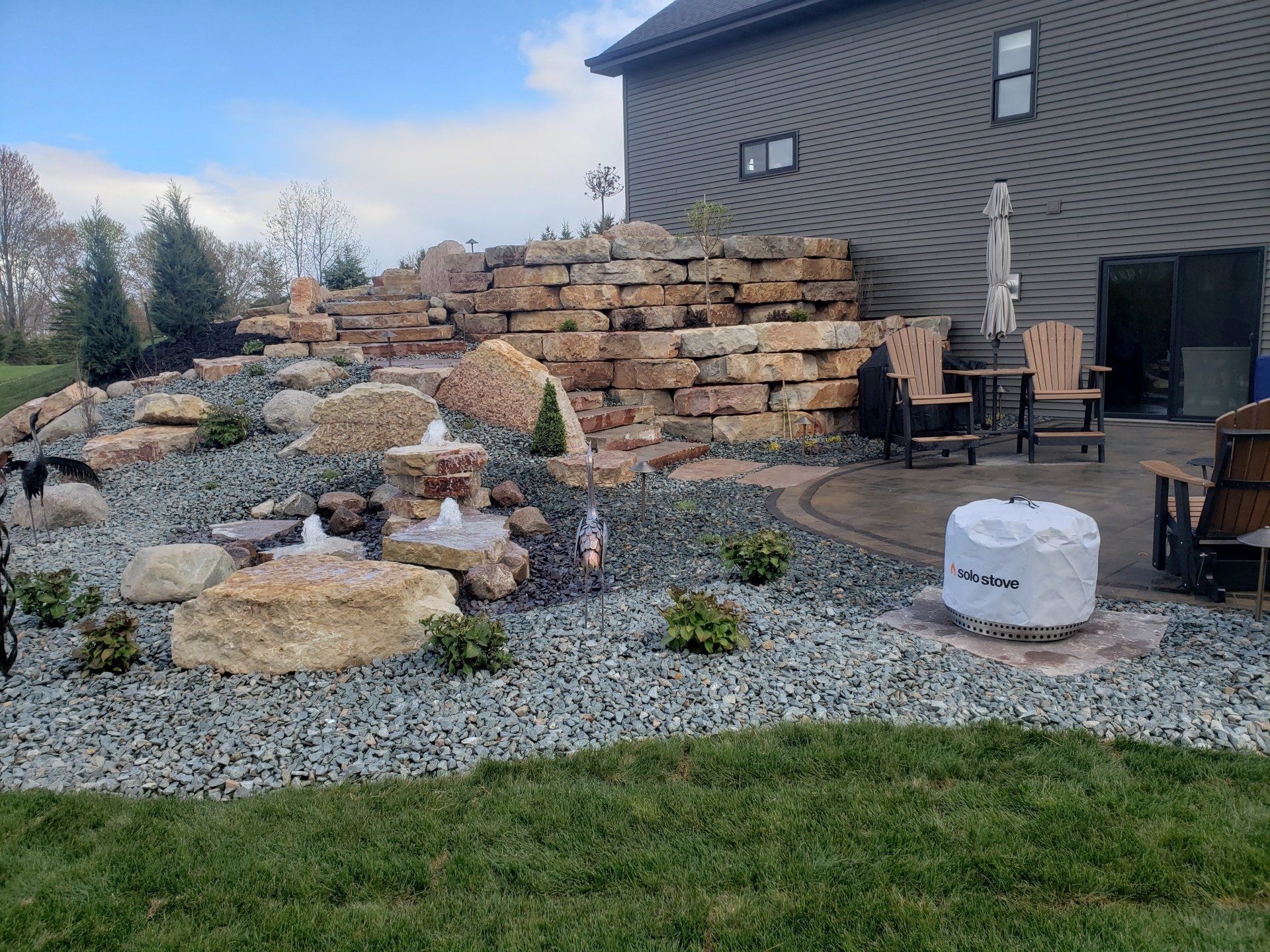 Landscaped backyard with waterfall, rock wall, patio, and fire pit.