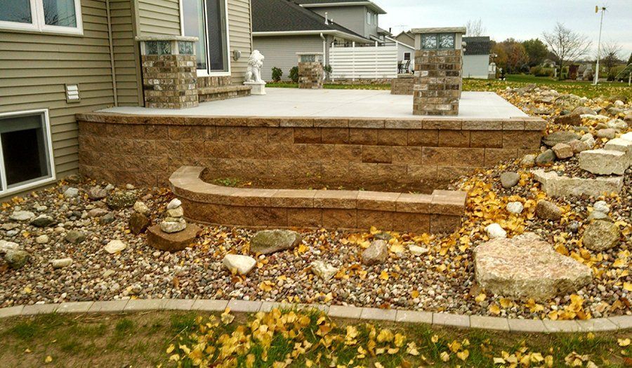 A raised stone patio with steps, gravel ground cover, and a house in the background.