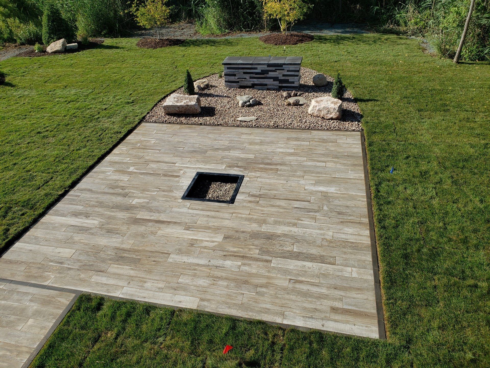 Patio with stone pavers and fire pit, surrounded by grass and rock garden.