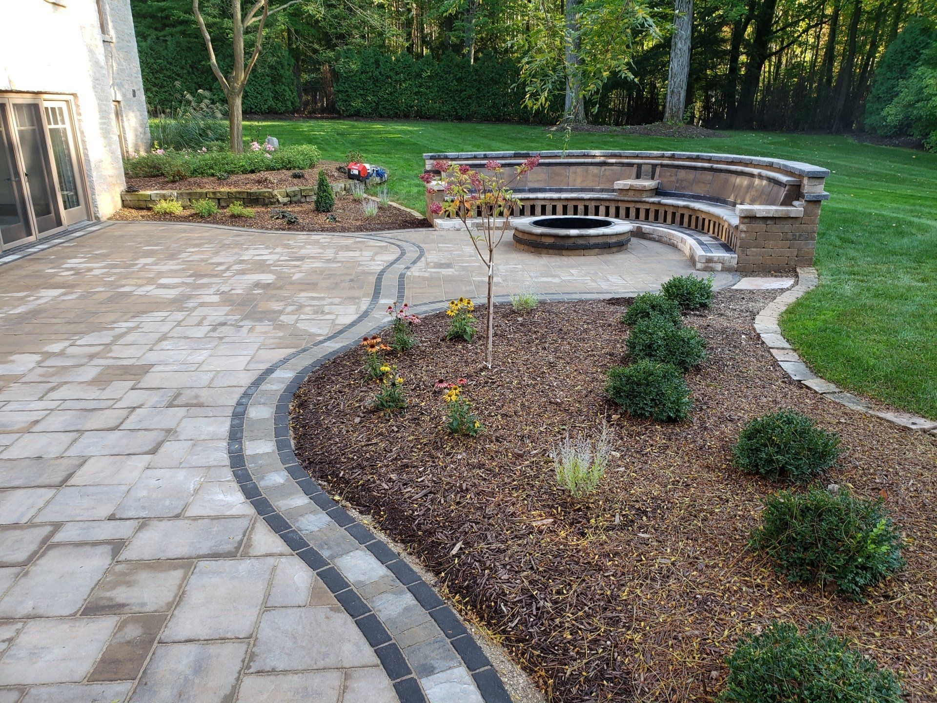 Patio with stone pavers, landscaping, fire pit, and built-in seating.
