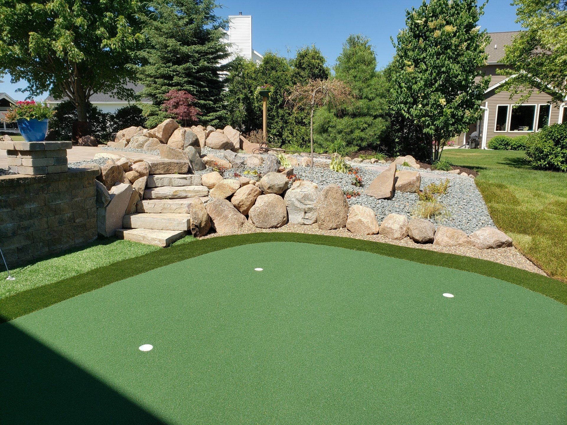 Green putting green with three holes, rock garden, stone steps, and landscaping.