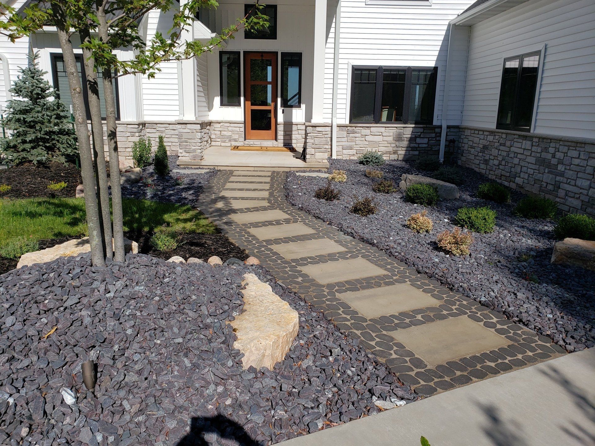 Stone pathway leading to a white house with a brown door, surrounded by dark gray gravel landscaping.