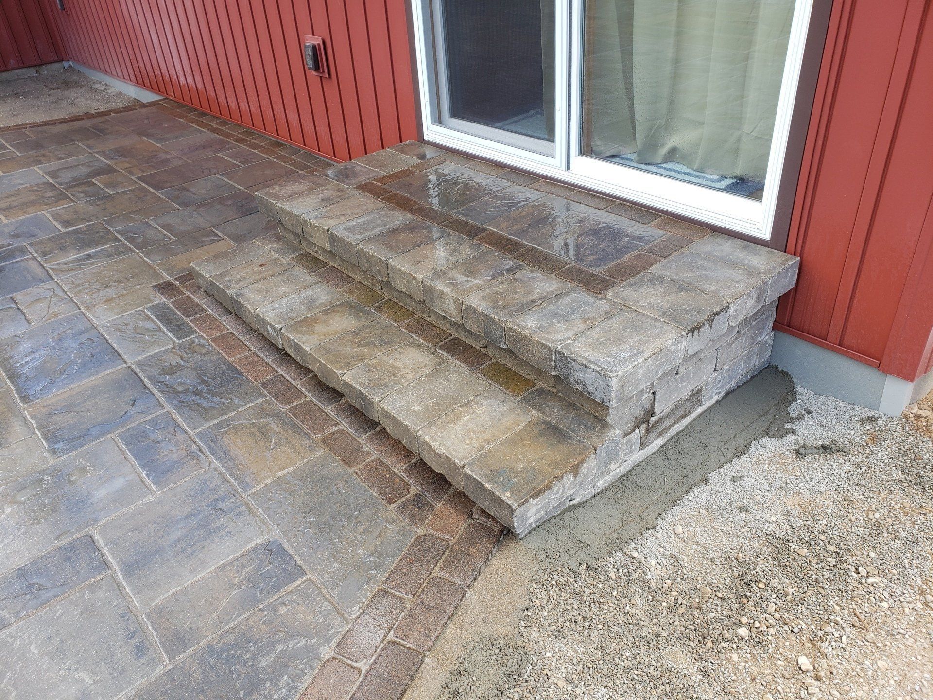Stone steps and patio with sliding door beside a red building.