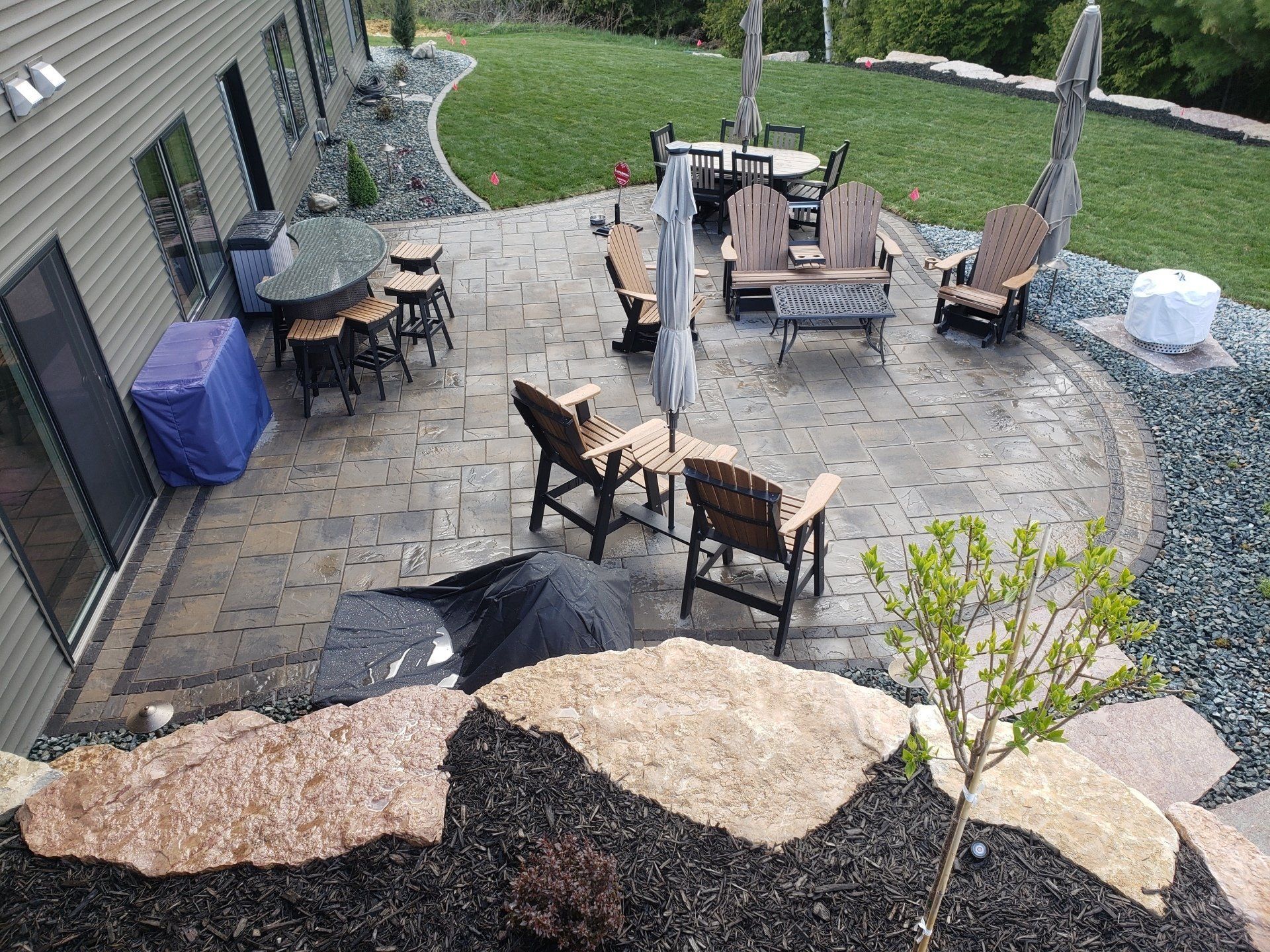 Patio with seating, umbrellas, and dining area next to a house with a green lawn.