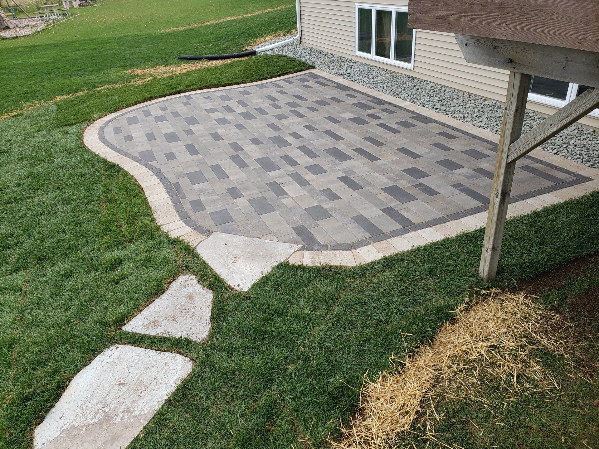 Brick patio with grass border, stepping stone path, and house with windows.