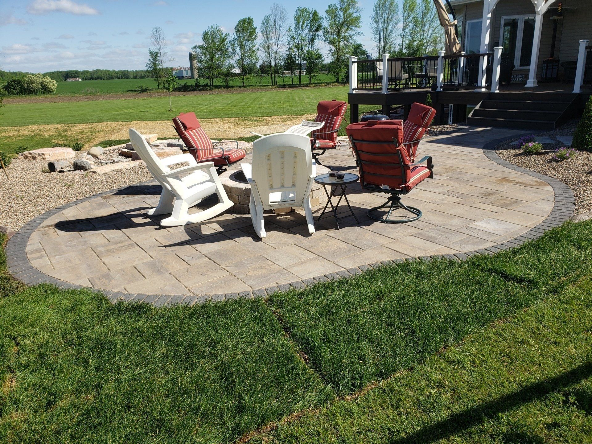 Fire pit area with seating on a stone patio, surrounded by grass.