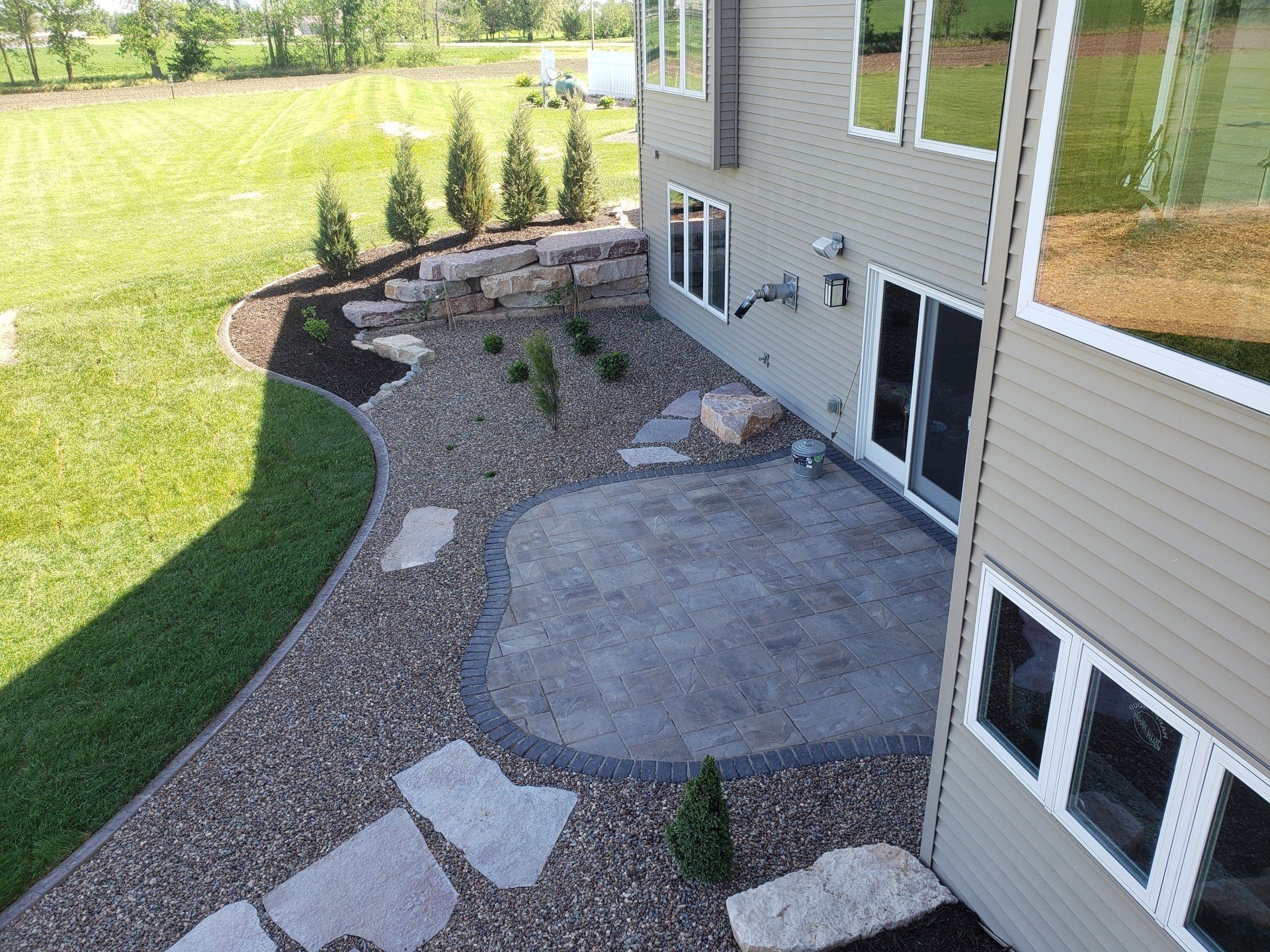 Backyard with patio, rock landscaping, and house with large windows.