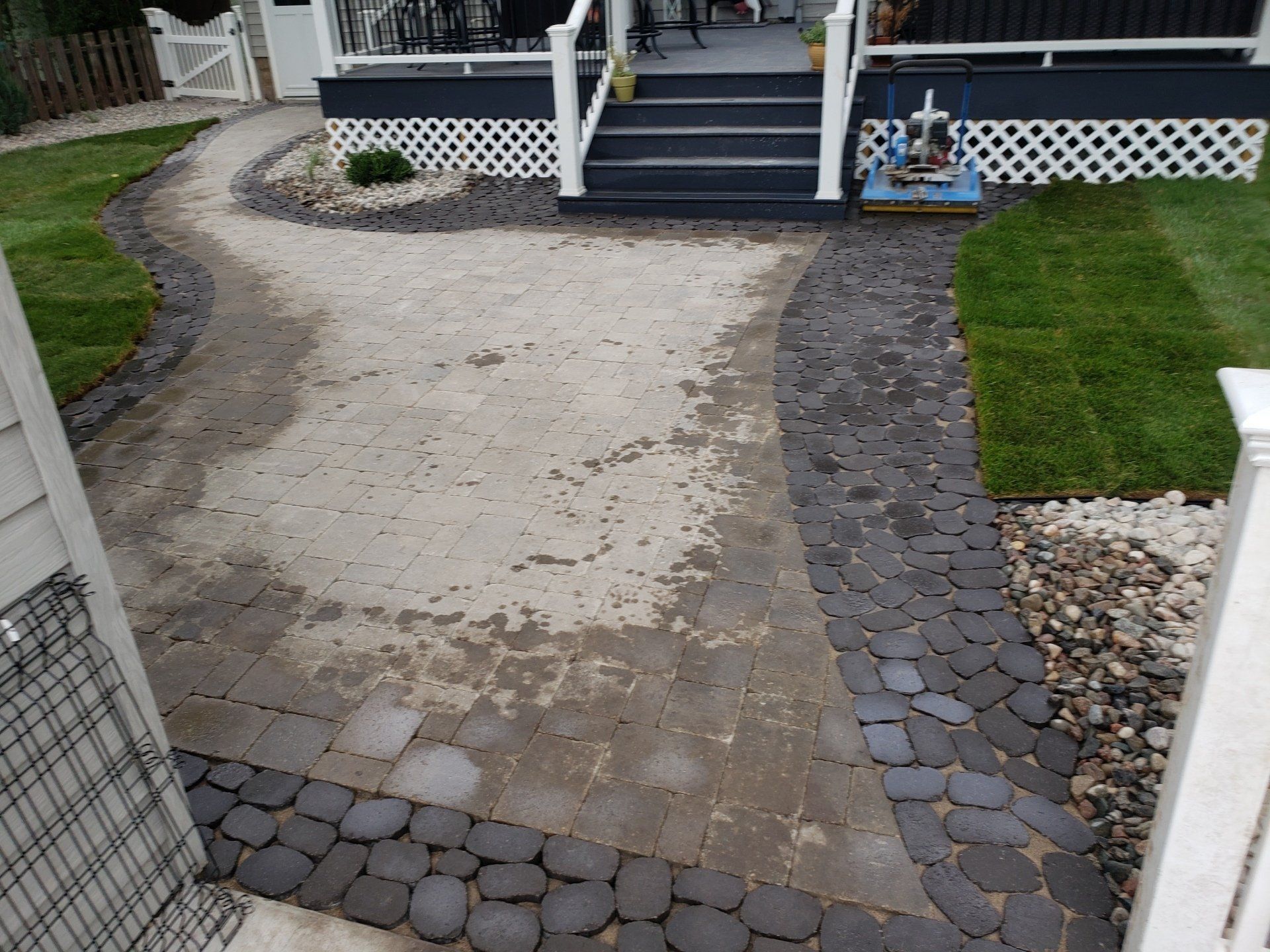 Pathway leading to a porch with black steps, lined with dark stones and green grass.
