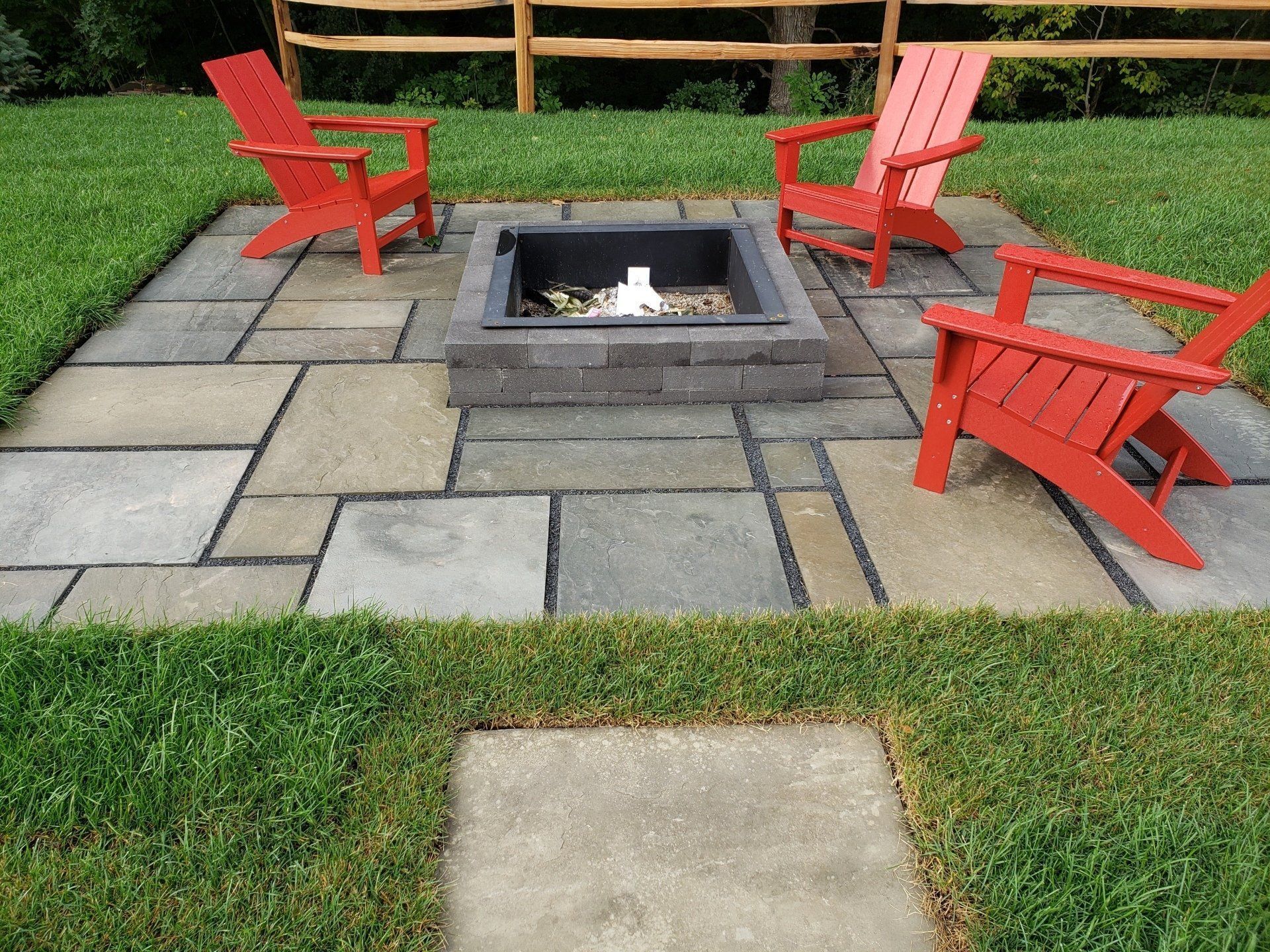 Fire pit patio with three red Adirondack chairs on a grassy lawn.